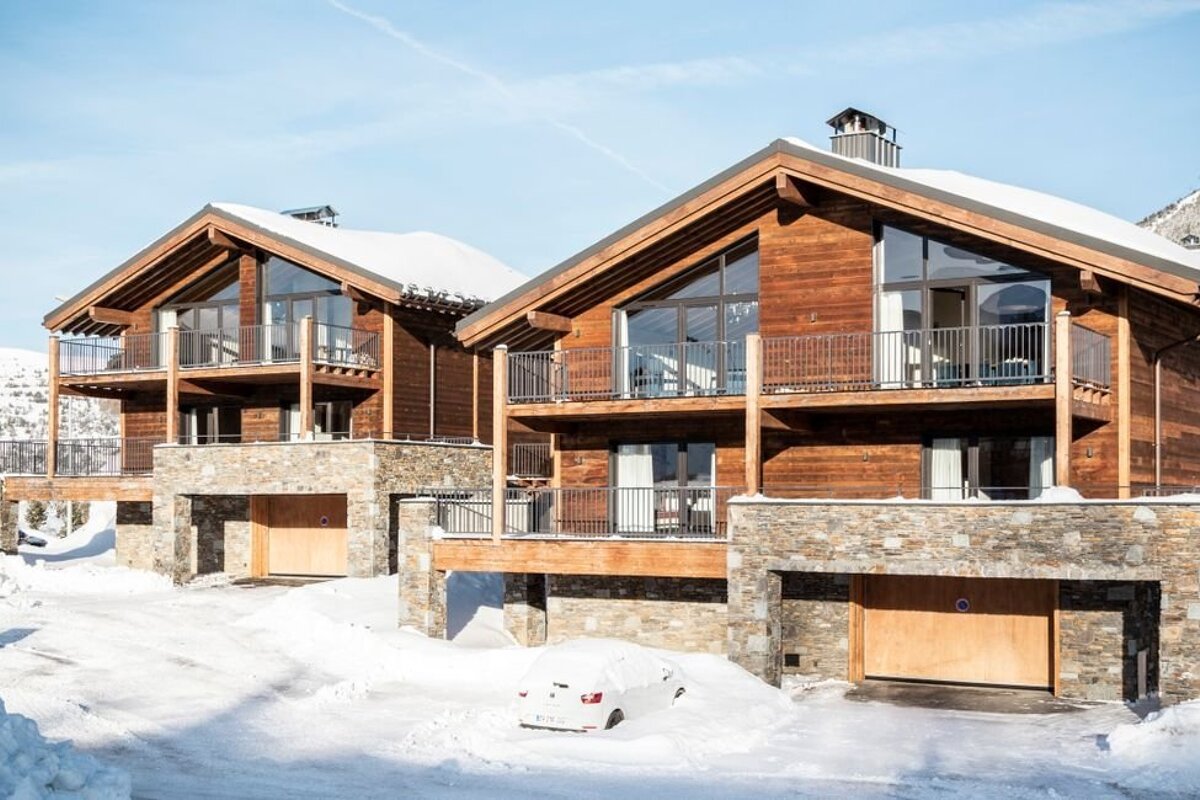 Two luxurious wooden chalets with stone bases nestled in a snowy winter landscape.