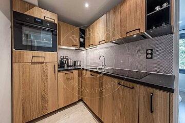 A modern kitchen with light wood cabinets, black countertops, a geometric tiled backsplash, built-in oven, sink, and stovetop.