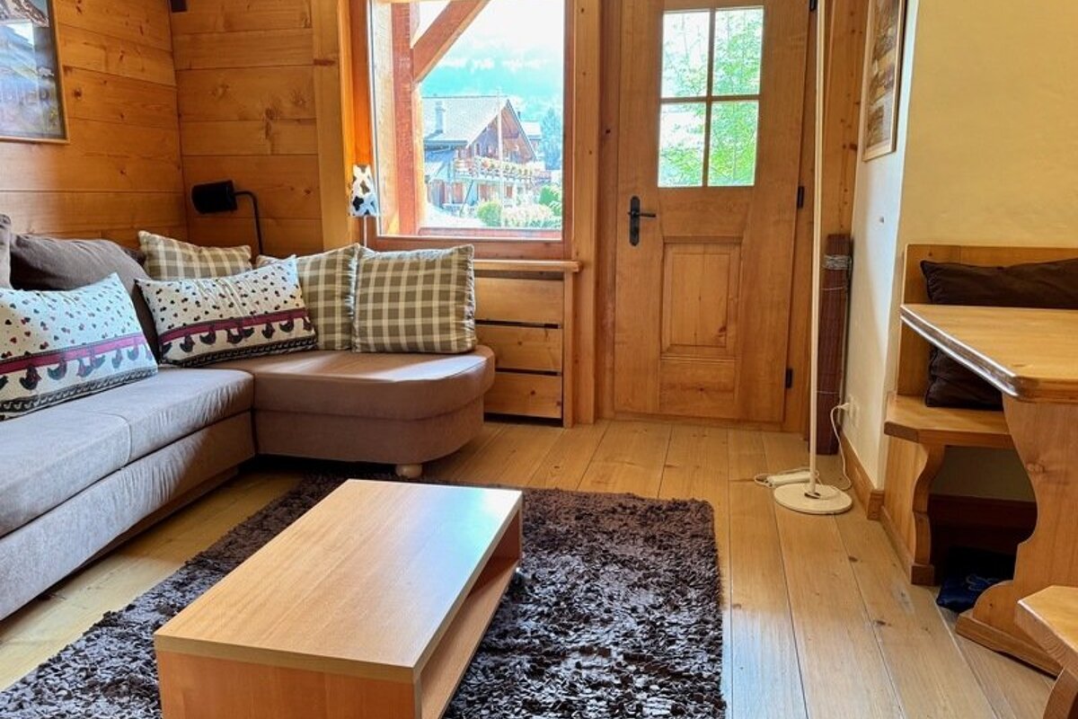 Cozy wooden cabin living room with a sectional sofa, decorative pillows, a low coffee table on a shag rug, and a rustic wooden door.