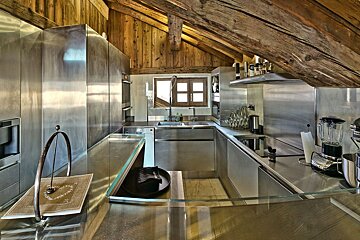 Sleek stainless steel kitchen under a rustic wooden beamed ceiling, contrasting modern design with natural textures.