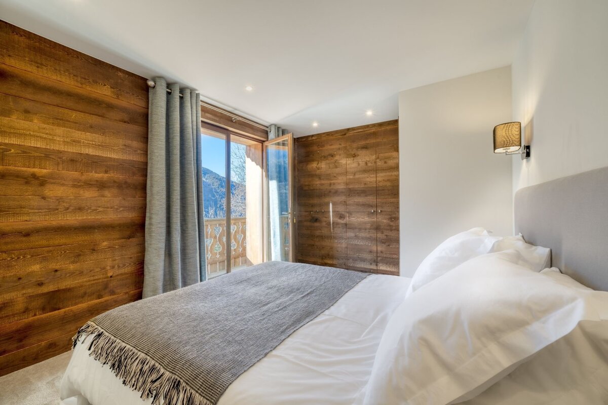 Modern bedroom with wood-paneled walls, built-in wardrobe, a comfortable bed, and a balcony offering stunning mountain views.