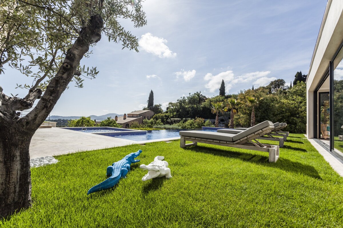A blue and white crocodile statue sits in the grass near a swimming pool