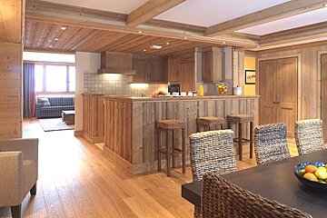 A spacious, open-plan chalet-style interior featuring a kitchen with a wooden island, dining area, and a living room, all richly paneled in natural wood.