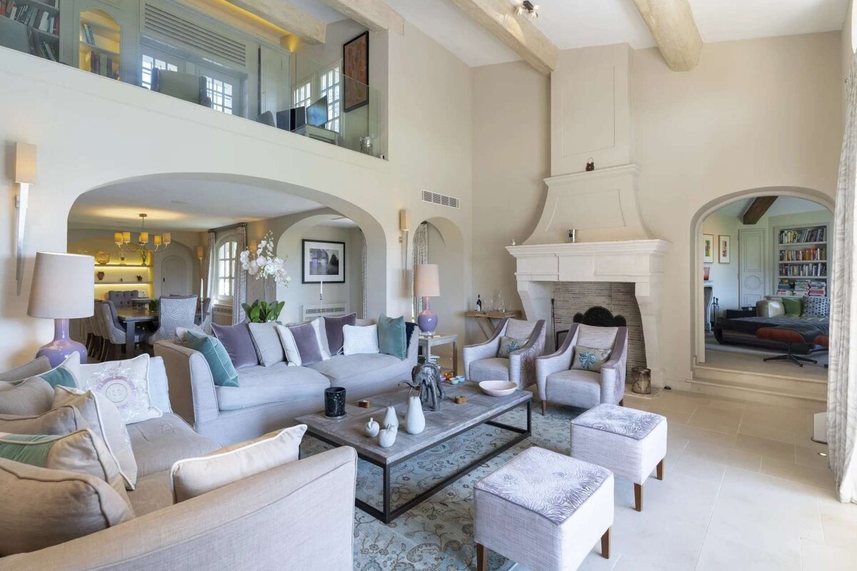 Spacious, elegant living room with neutral tones, arched entries, a grand fireplace, and an upper mezzanine overlooking plush seating.