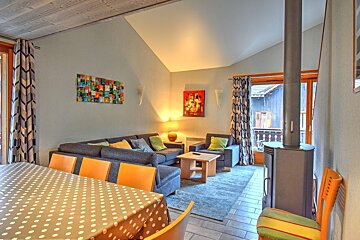 Bright, modern open-plan living/dining room features a grey sectional, vibrant art, a wood stove, and a polka-dotted dining table.