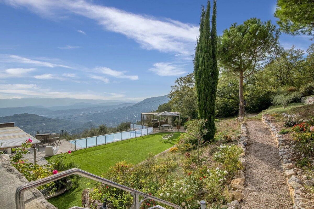 Luxury hillside garden with infinity pool, green lawn, and pergola, offering breathtaking panoramic views of distant mountains under a blue sky.