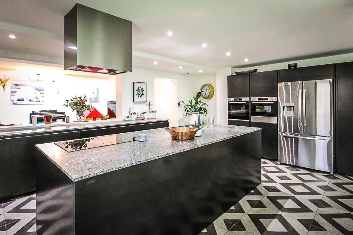 A modern kitchen with dark cabinetry, gray granite counters, stainless steel appliances, a large island, and a distinctive black and white geometric floor.