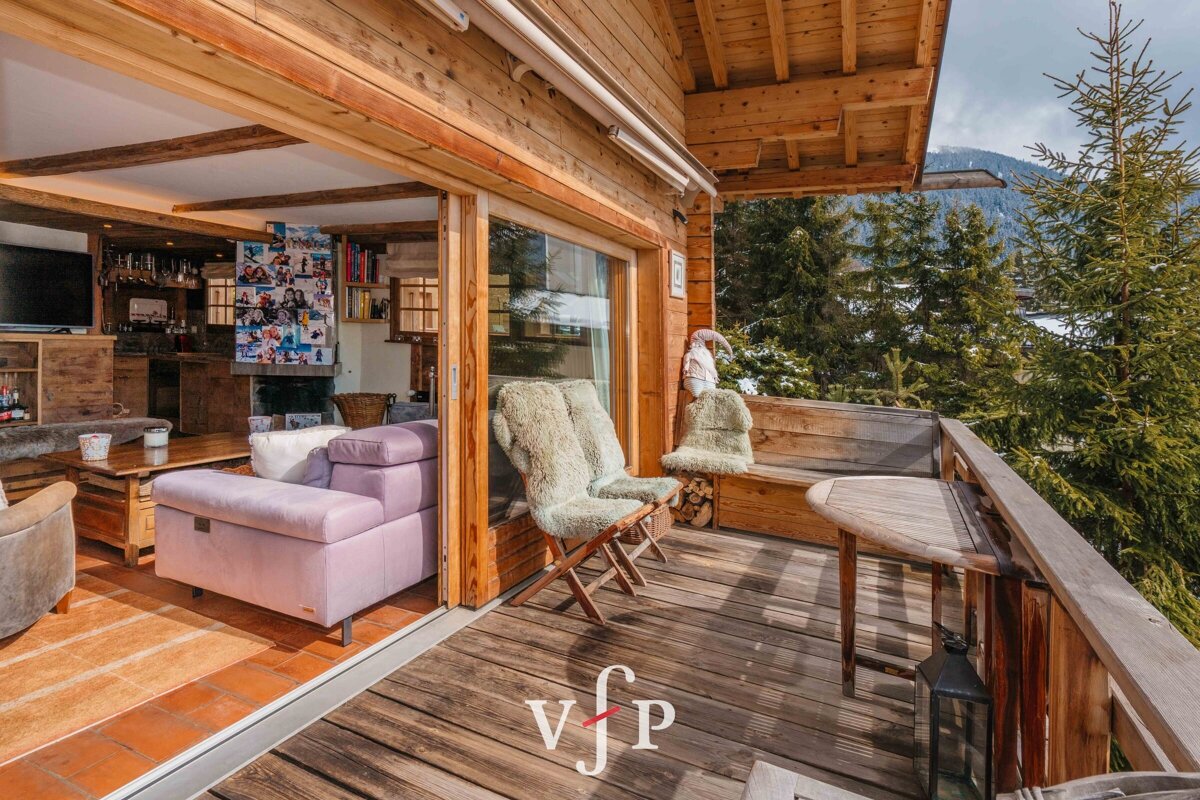 Cozy wooden chalet featuring a living room that opens onto a balcony with sheepskin chairs and scenic forest views.