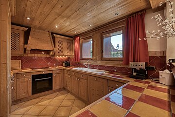 Cozy, rustic kitchen with wooden cabinets, wood ceilings, red and yellow tiled countertops, and red curtains.
