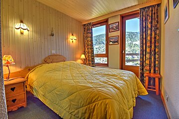 Cozy chalet bedroom with wood paneling, a large yellow-quilted bed, and windows looking out onto scenic mountain views.