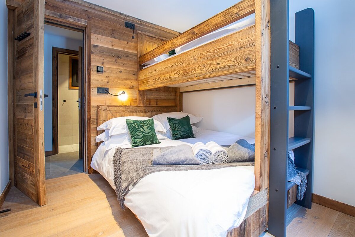 A wooden bunk bed with white sheets and green pillows