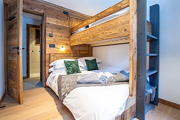 A wooden bunk bed with white sheets and green pillows