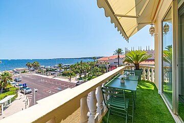 A sunny balcony with artificial grass and green furniture overlooking a coastal road and the blue ocean.