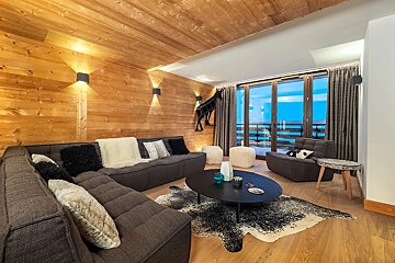 A modern, rustic living room featuring wood-paneled walls, large sectional sofas, a black coffee table, and an animal-print rug.