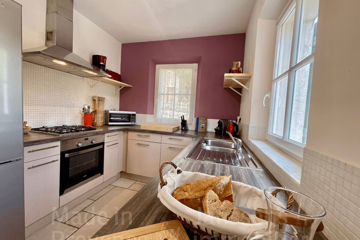 A functional kitchen featuring white cabinets, a burgundy accent wall, and modern appliances. A basket of bread rests on the dark countertop.
