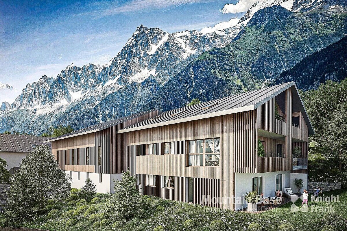 A modern wooden building with large windows sits nestled in a lush green landscape, backed by towering snow-capped mountains.