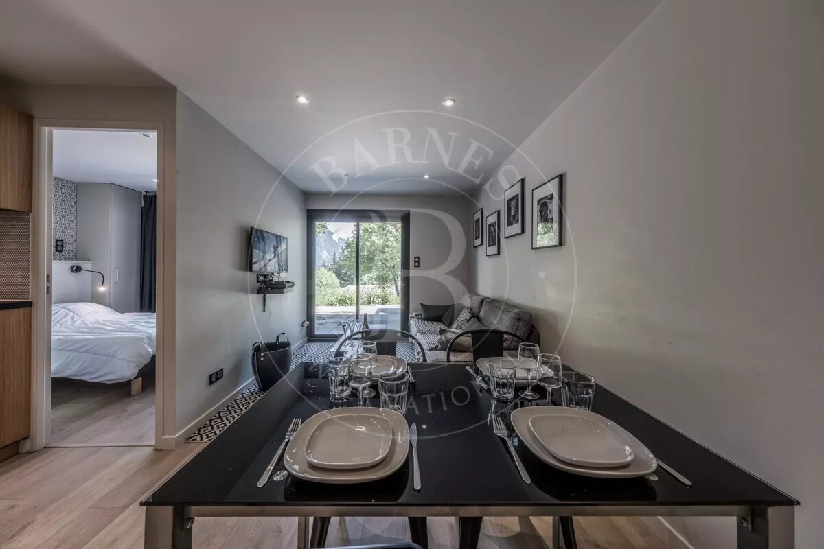 Modern apartment with a dining table set, a living area featuring a sofa, TV, and patio view, and a partial glimpse of an adjacent bedroom.