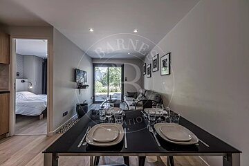Modern apartment with a dining table set, a living area featuring a sofa, TV, and patio view, and a partial glimpse of an adjacent bedroom.