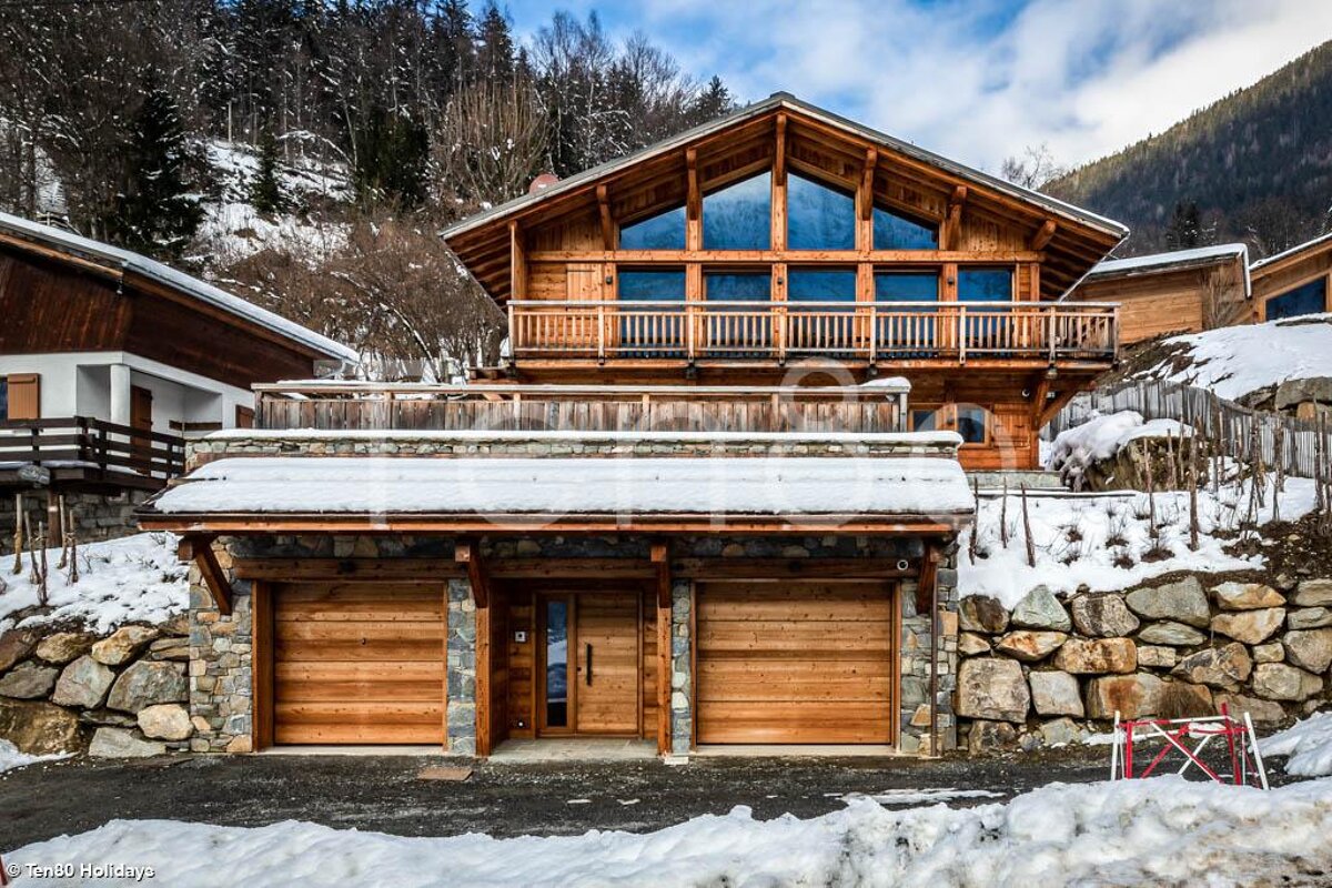 A large wooden house is surrounded by snow and rocks
