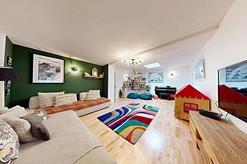 A bright, eclectic family room with a green accent wall, varied seating, a colorful rug, piano, bookshelves, and kid-friendly play areas.