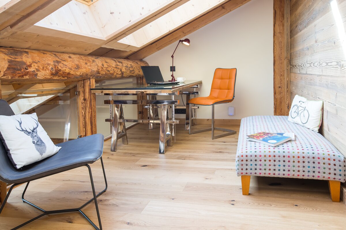A chair with a deer pillow sits next to a desk with a laptop on it