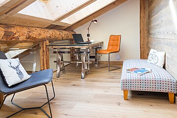A chair with a deer pillow sits next to a desk with a laptop on it