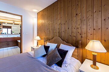 A bedroom with wood paneling and a bed and two lamps