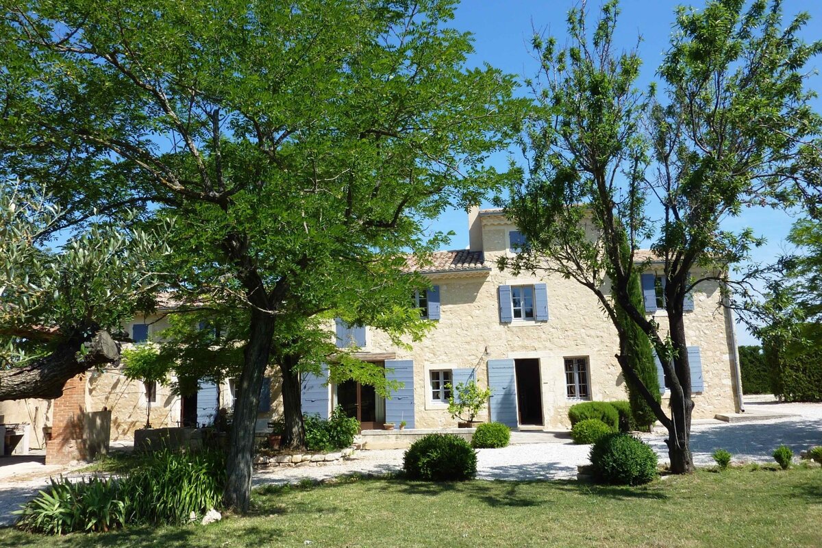 A house with blue shutters is surrounded by trees and bushes