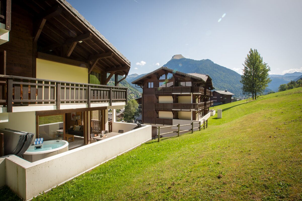 A hot tub sits outside of a house with mountains in the background
