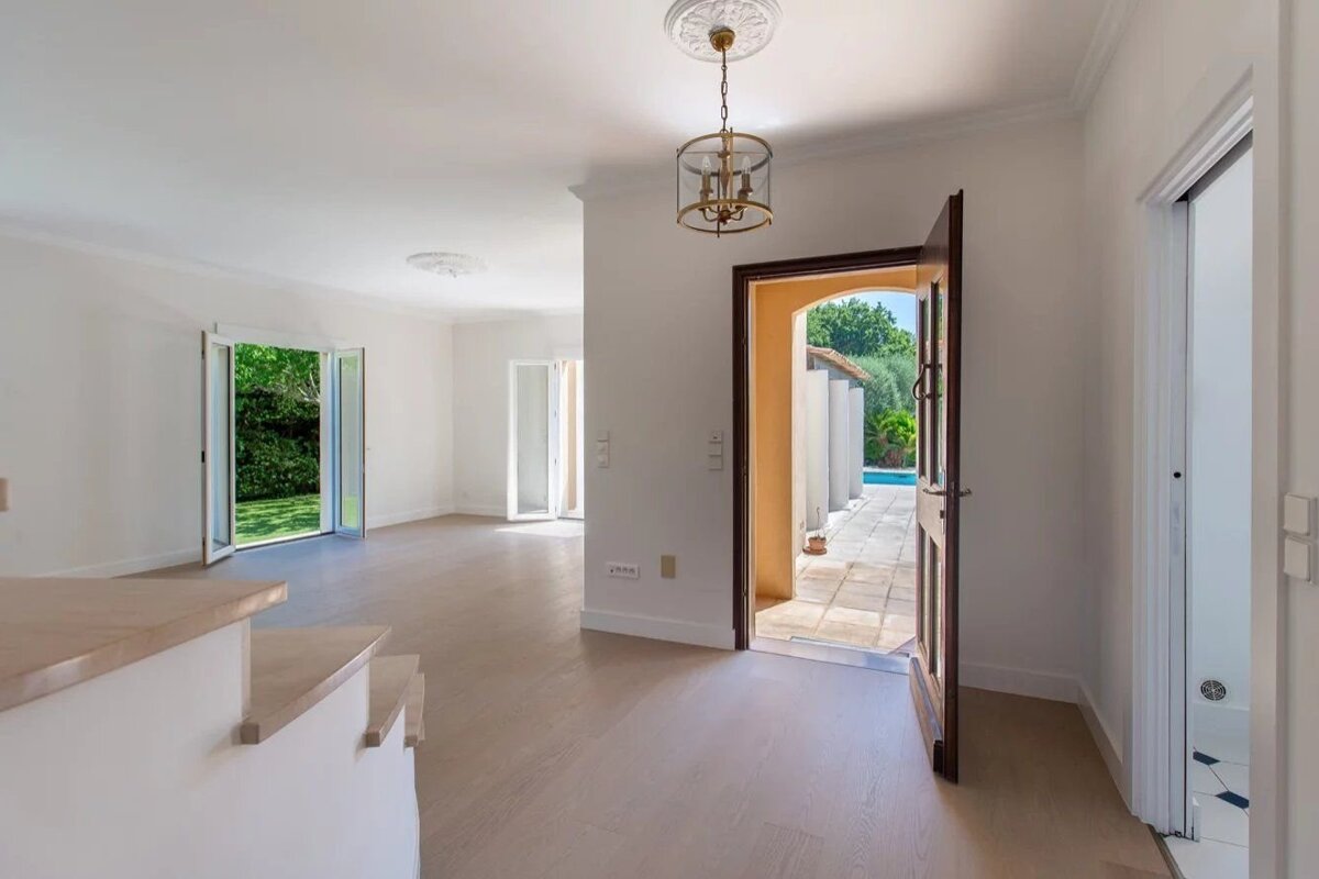 Bright, empty entryway with light wood floors, an open front door leading to a patio, and French doors opening to a lush garden.