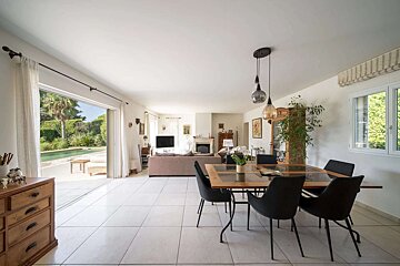 Bright, open-concept living and dining room with white tile flooring, a modern dining set, and a comfortable living area, all opening to a pool deck.
