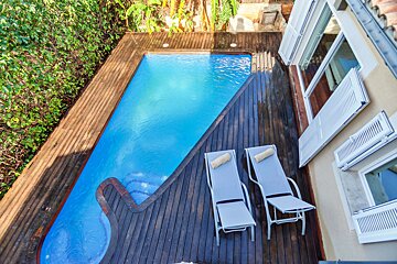 Two lounge chairs sit on a wooden deck next to a swimming pool