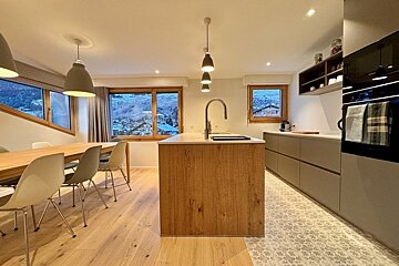 Modern kitchen and dining area with warm wood finishes, sleek grey cabinets, and scenic snowy mountain views through the windows.