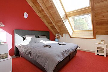 A bedroom with red walls and a gray bed