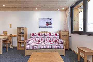 A cozy, wood-paneled room with a red and white patterned sofa, a picture of ski gondolas, and a window looking out onto a snowy scene.