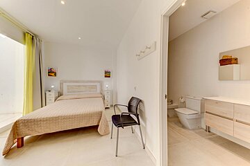 A bedroom with a bed and a chair next to a bathroom