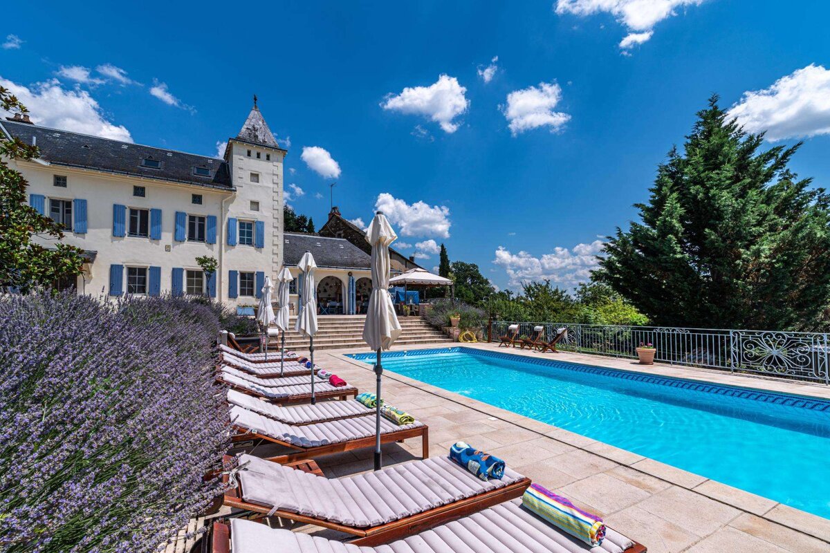 A large white building with blue shutters sits behind a large swimming pool