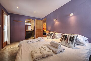 A bedroom with purple walls and feather pillows on the bed