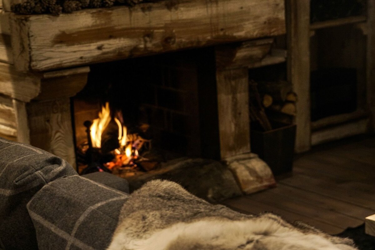 A cozy, rustic scene featuring a roaring fireplace, a plaid sofa arm, and a soft fur blanket, creating a warm and inviting atmosphere.