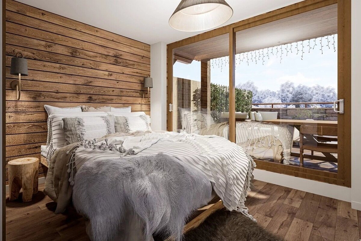 Cozy cabin bedroom with wood-paneled walls, plush bedding, and large sliding glass doors opening to a winter balcony.