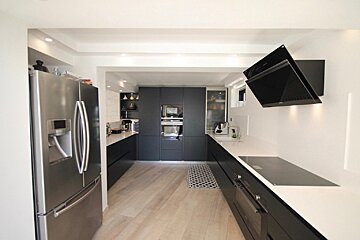 A kitchen with black cabinets and a stainless steel refrigerator