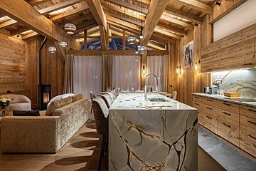 A luxurious, open-plan wooden chalet interior with vaulted ceilings, a modern marble kitchen island, cozy living area with fireplace, and dining space.