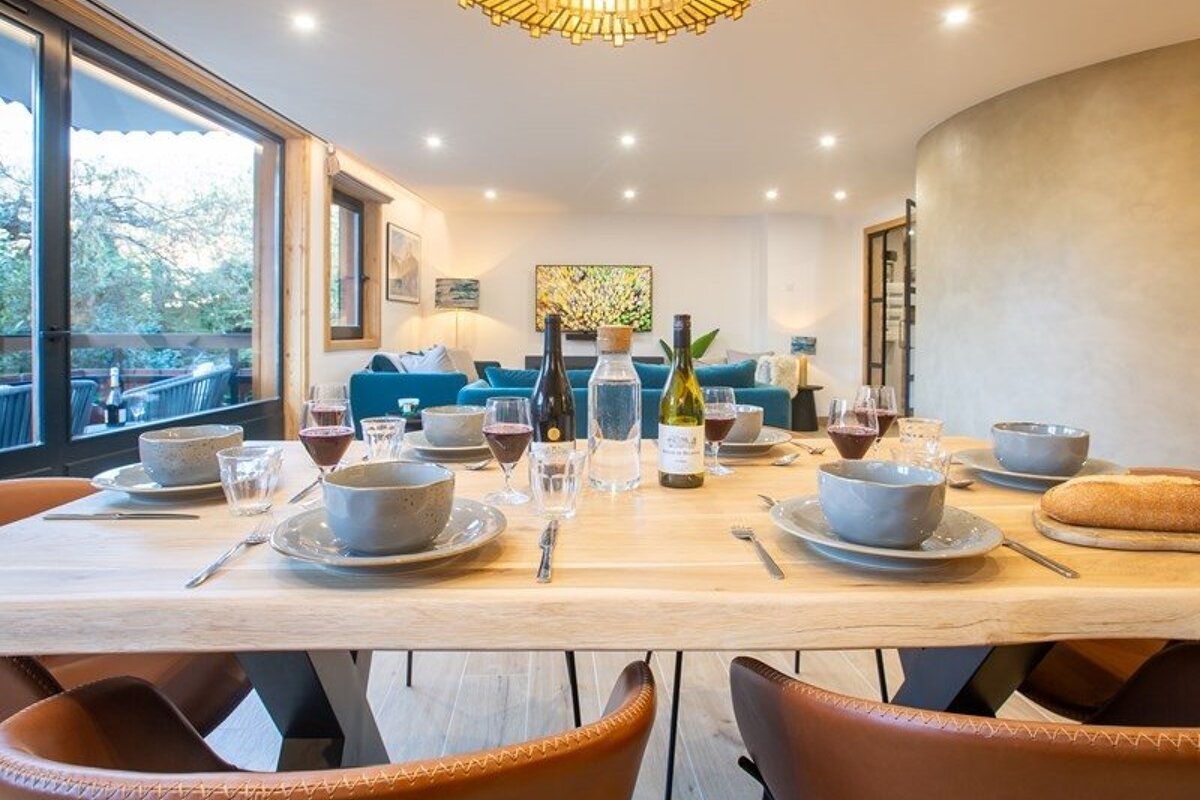 Modern dining table set with plates, bowls, and wine bottles, overlooking a living room with a blue sofa.