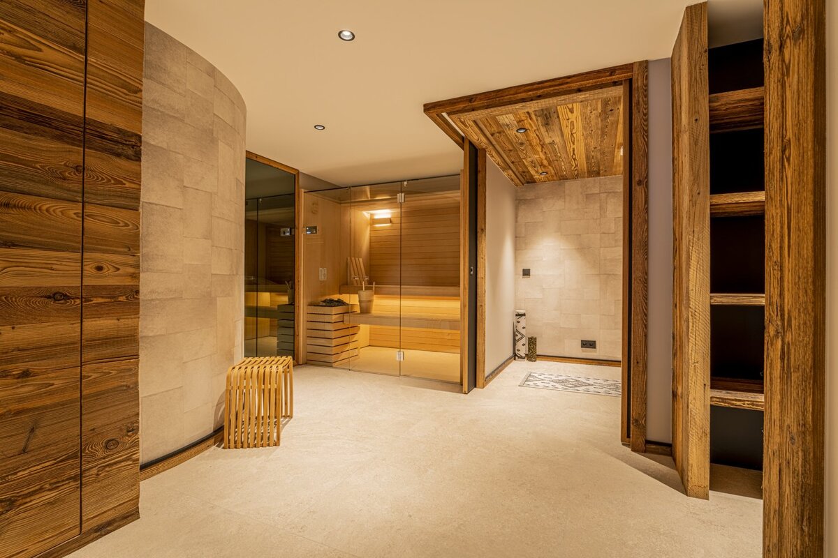 Modern wellness area featuring a glass-enclosed wooden sauna, warm stone tile flooring, and rustic wood accents.
