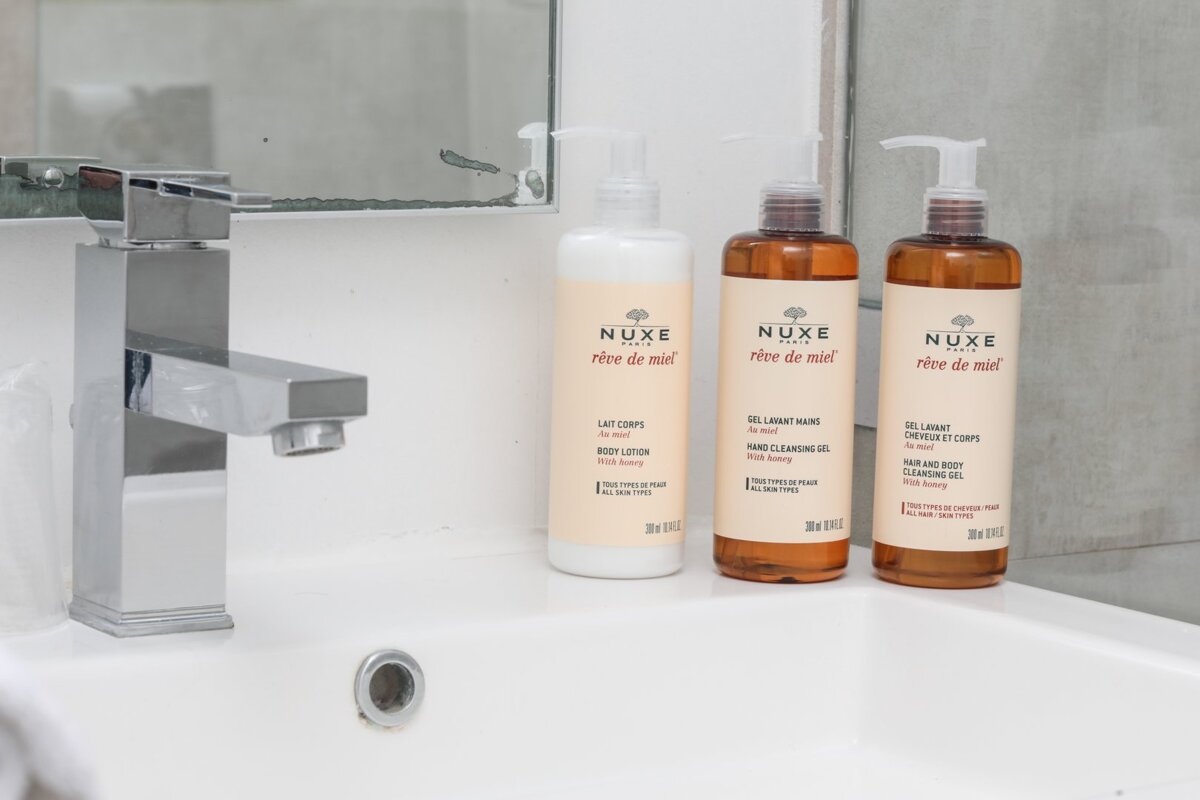 Three bottles of nuxe reve de miel are on a bathroom sink