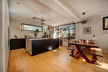Modern, open-plan kitchen and dining area with a large black island, light wood floors, rustic dining table, and scenic windows.