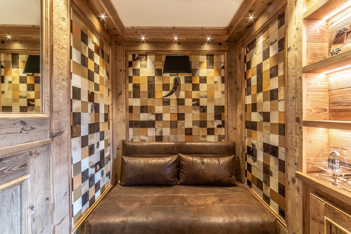 A cozy, wood-paneled nook features a brown leather banquette, chequered hide walls, a horn-shaped wall lamp, and spotlights.