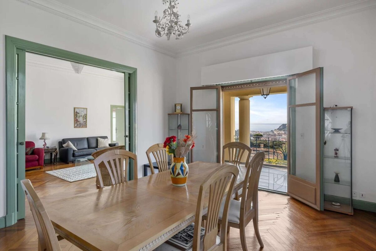 Spacious dining room with a wooden table, chairs, and a chandelier. Features include a stunning sea-view balcony and an adjoining living room.