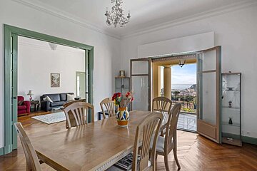 Spacious dining room with a wooden table, chairs, and a chandelier. Features include a stunning sea-view balcony and an adjoining living room.