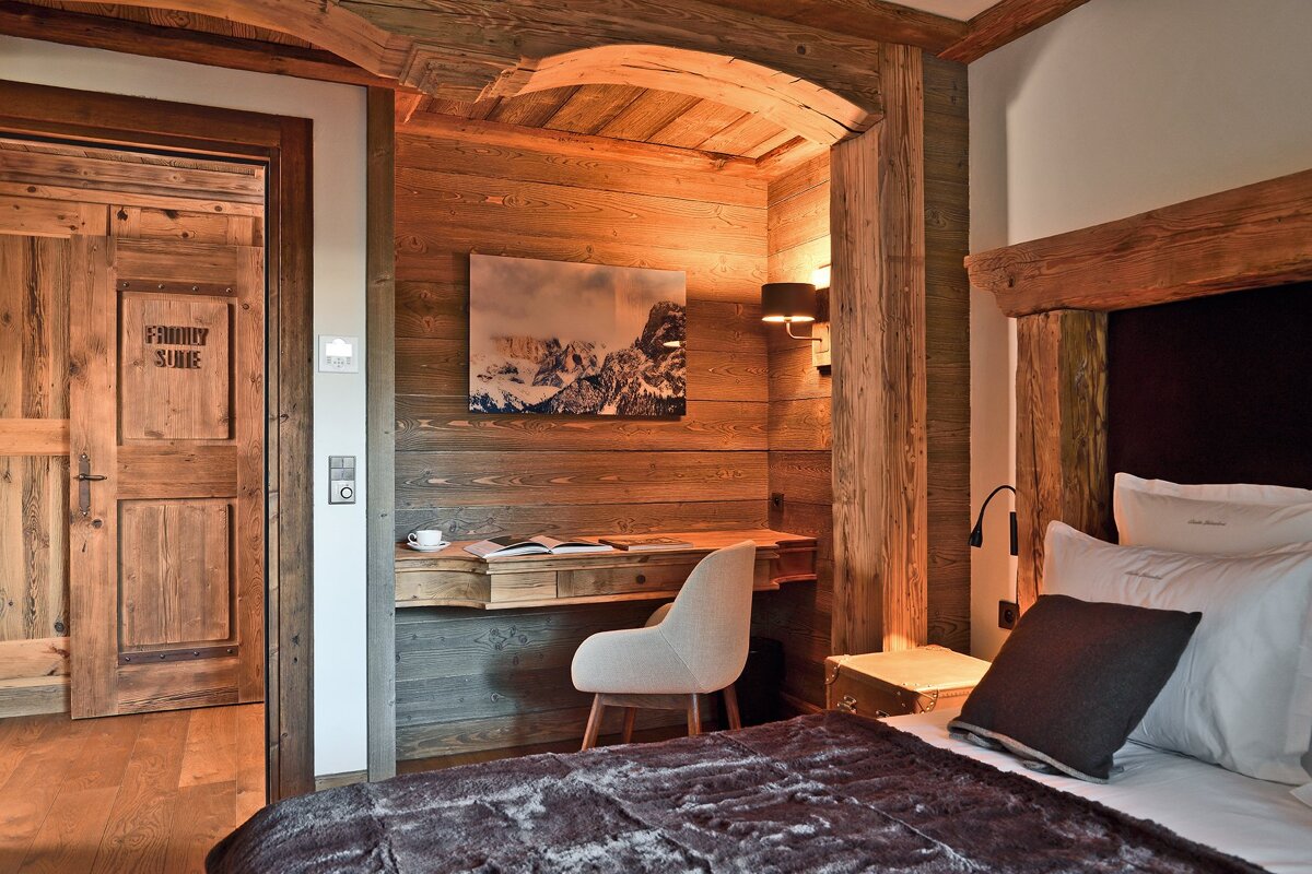 A warm, rustic wooden bedroom featuring a bed, a desk area with mountain art, and a door marked 